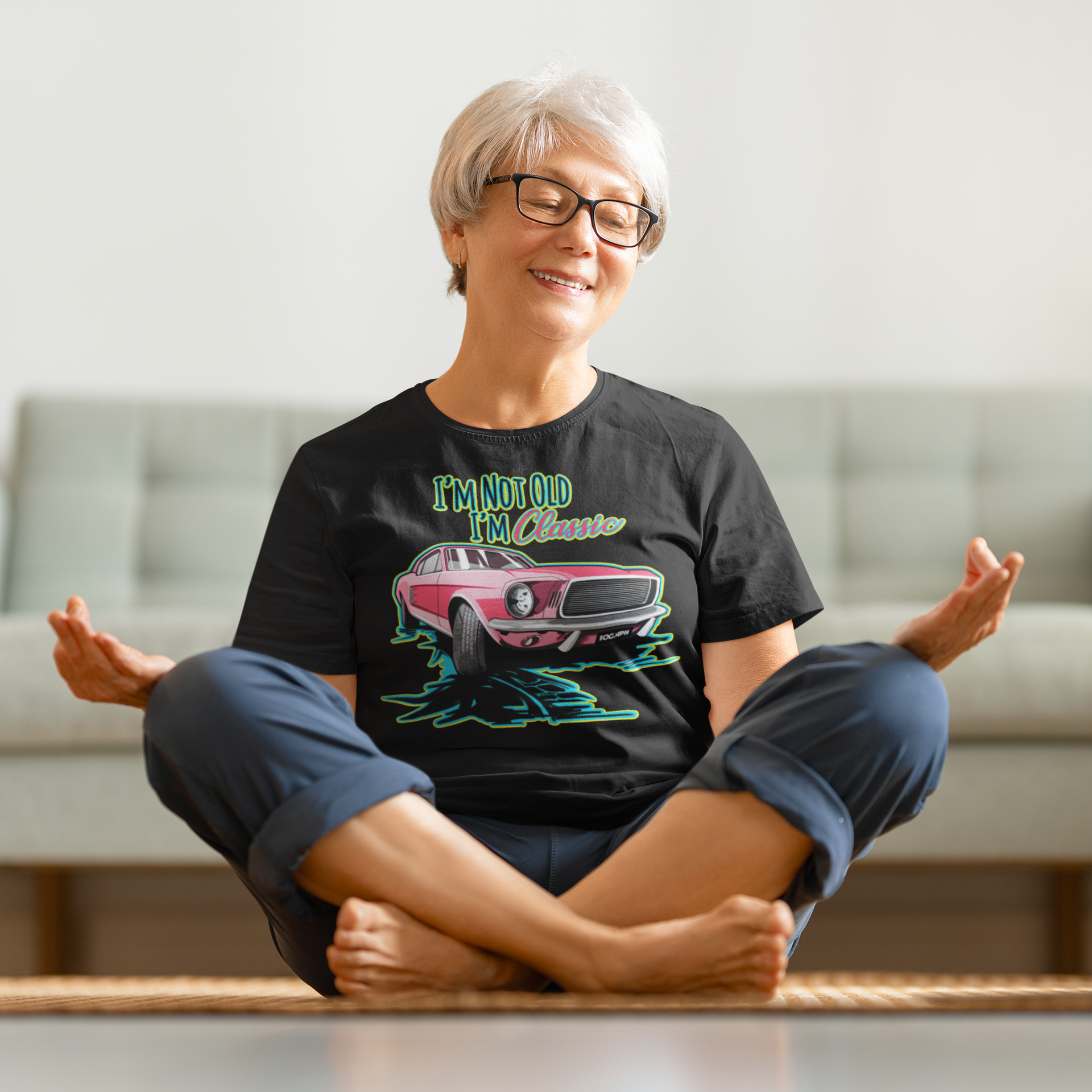 A middle age woman practicing yoga while wearing a tee shirt with an image of a Ford Mustang, and text reading "I'm not old, I'm Classic"