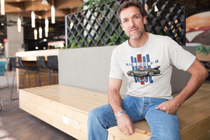 A man sitting on a bench in a restaurant, he's wearing a white tee shirt with an image of a Porsche and text that reads "Air Cooled".