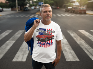A man standing in the middle of the road, with a jacket over his shoulder. He is wearing a white tee shirt with the image of a Mustang muscle car. The shirt has text that reads "American Made, World Class".