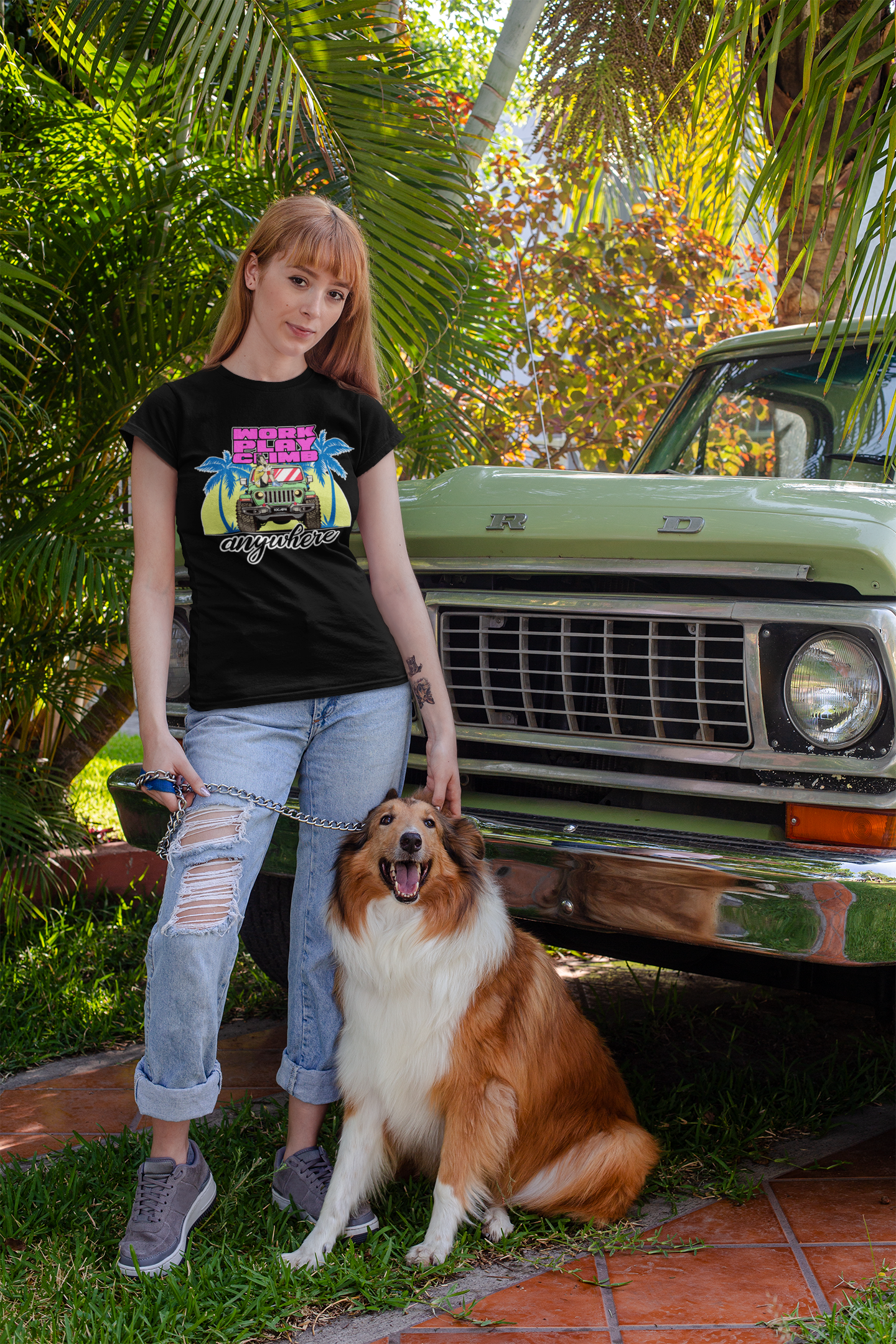 Image of A woman standing with her dog in front of a truck. She is wearing a black tee shirt with the image of a Jeep Wrangler, and text reading 