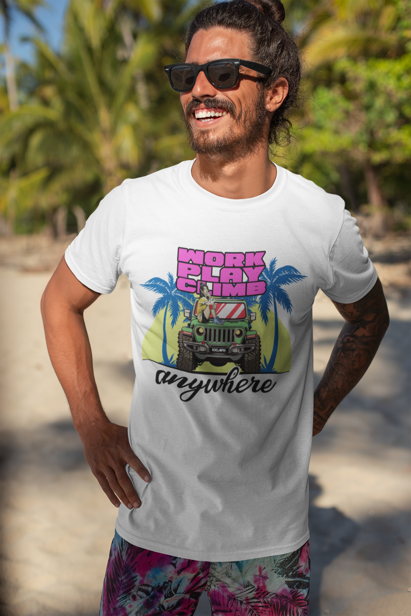 Image of A man standing on a beach and smiling, while wearing a white tee shirt with the image of a Jeep Wrangler, and text reading 