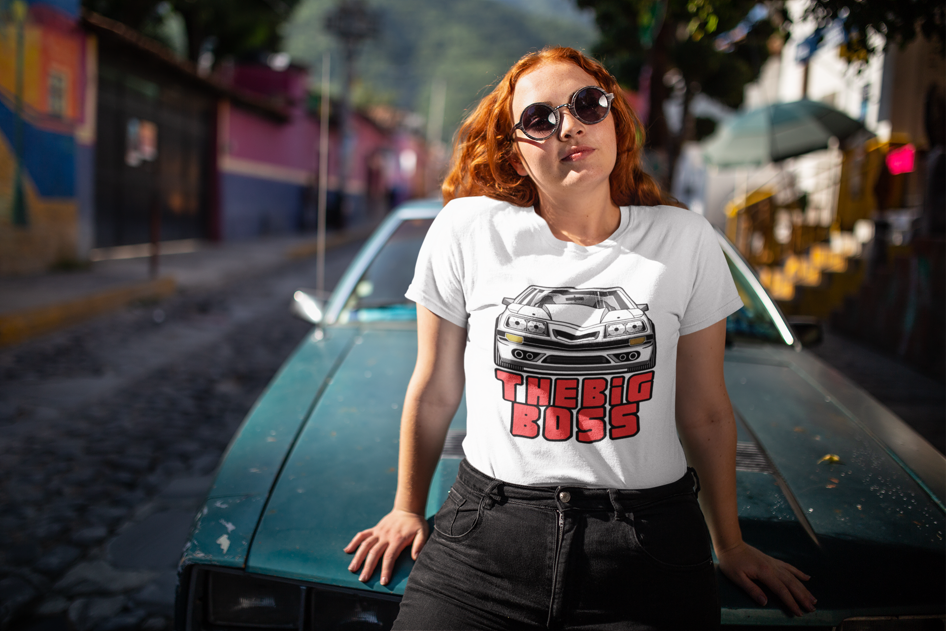 Image of A woman leaning against a car, while wearing a white tee shirt with an image of a Ford Mustand Foxbody, and text reading 