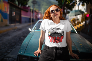 A woman leaning against a car, while wearing a white tee shirt with an image of a Ford Mustand Foxbody, and text reading "The Big Boss"