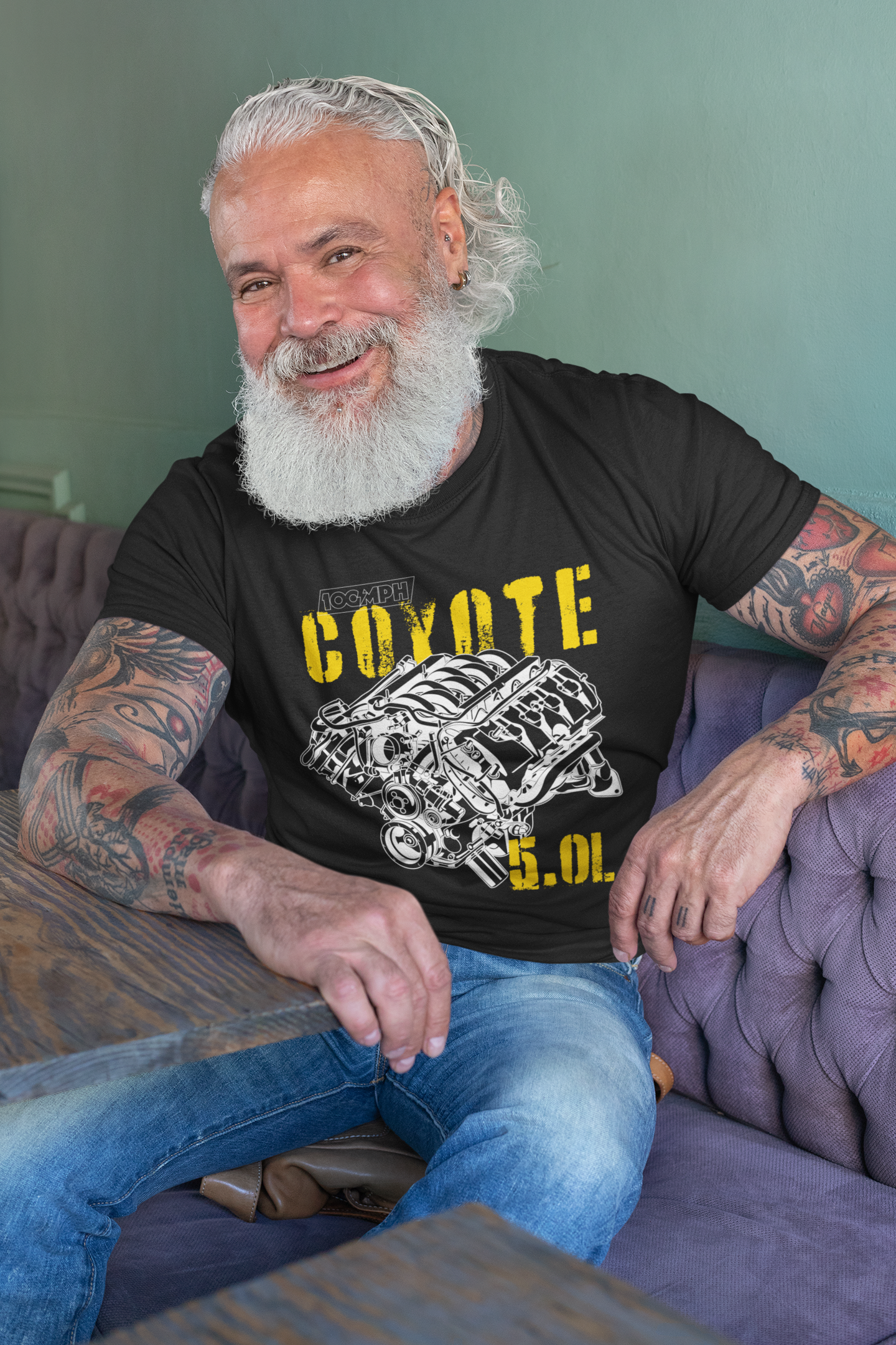 Image of A man sitting in a restaurant leaning against a table. He's wearing a black tee shirt with an image of a Coyote engine. The tee shirt has text that reads 
