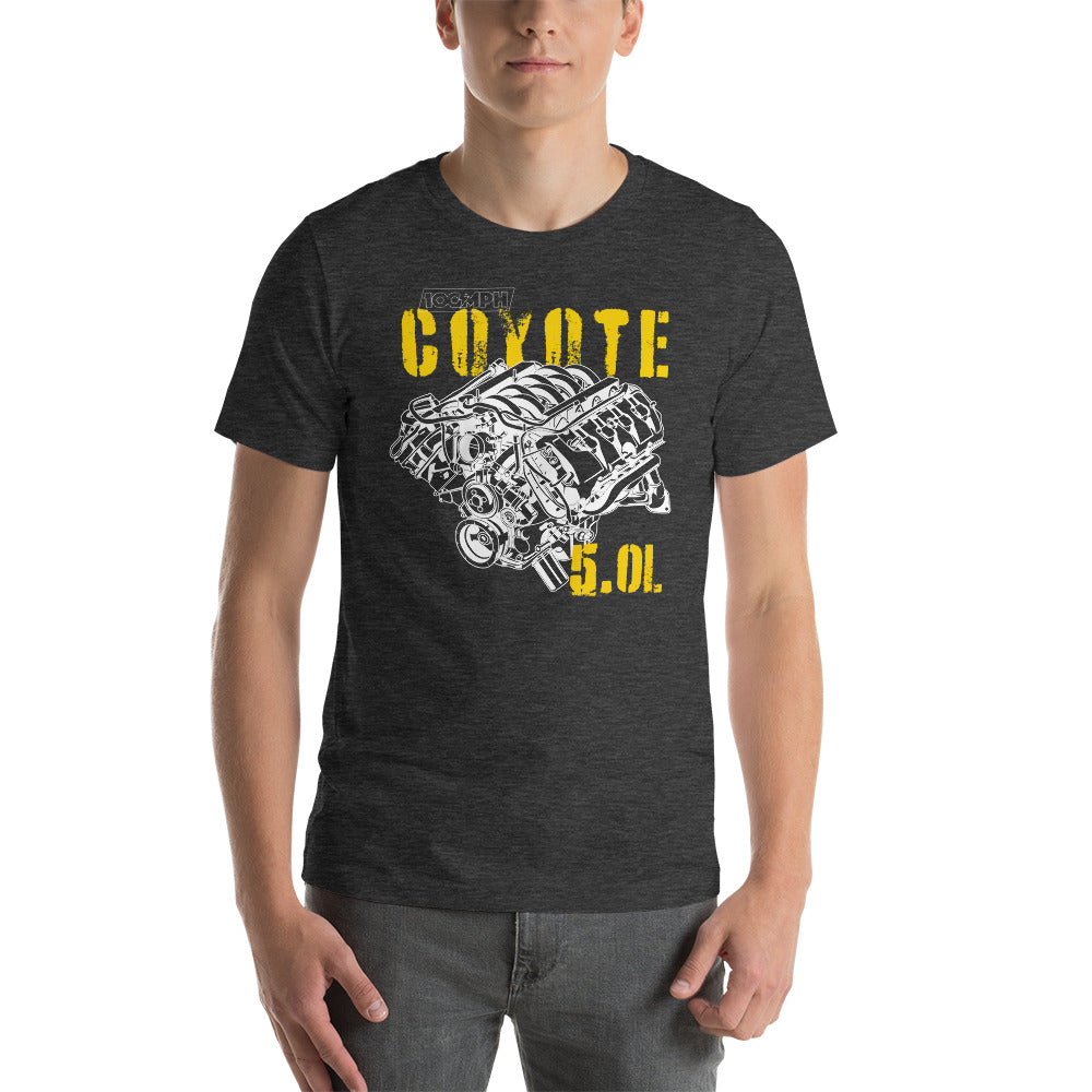 Image of A man standing. He's wearing a dark grey tee shirt with an image of a Coyote engine. The tee shirt has text that reads 