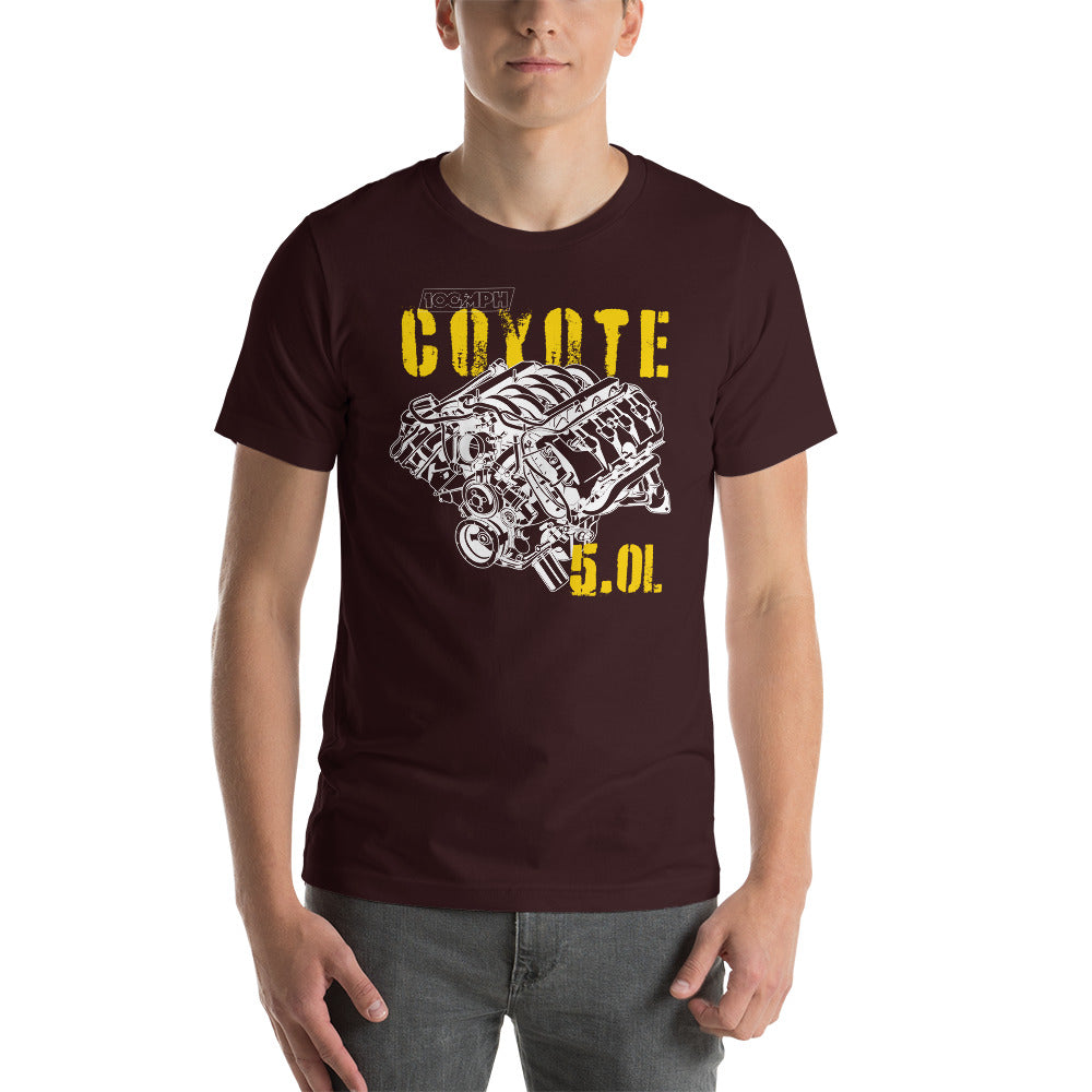 Image of A man standing. He's wearing an oxblood red tee shirt with an image of a Coyote engine. The tee shirt has text that reads 