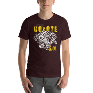 A man standing. He's wearing an oxblood red tee shirt with an image of a Coyote engine. The tee shirt has text that reads "Coyote 5.0L". 